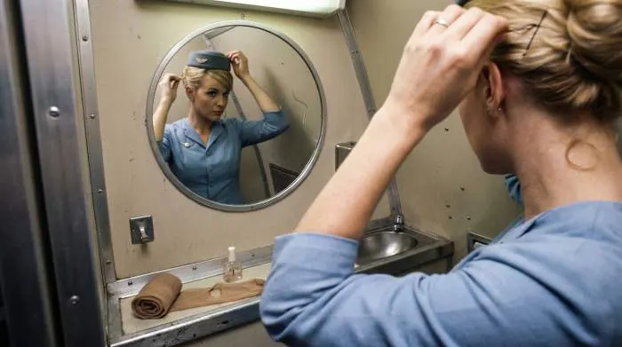 1960s flight attendant fixing hair and stockings in cramped airplane lavatory using grooming skills