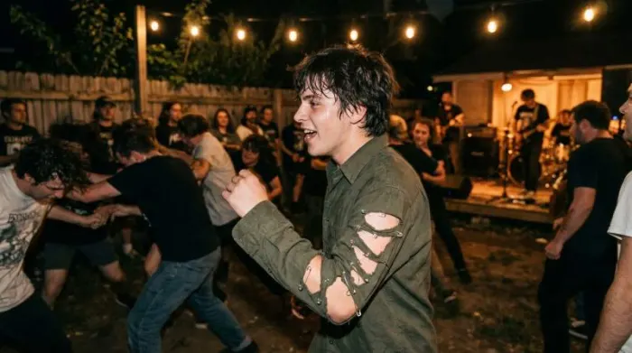 Young person wearing ripped button-down with safety pins at backyard show showing modern punk style in real life