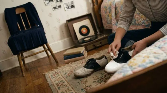 Teen polishing black-and-white saddle shoes in 1950s bedroom Teen polishing black-and-white saddle shoes in 1950s bedroom